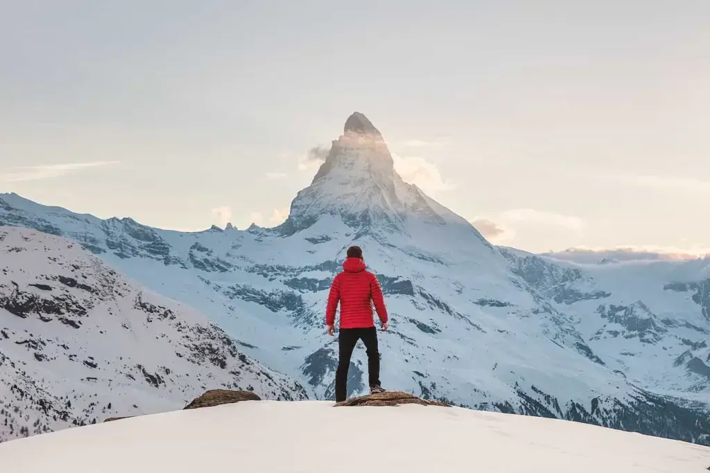 person in red hoodie standing on snowy mountain during daytime