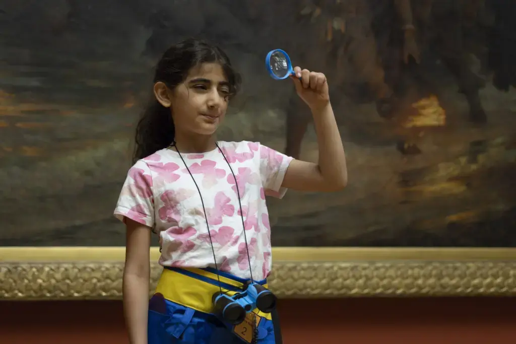 A child examines a gallery painting through a magnifying glass